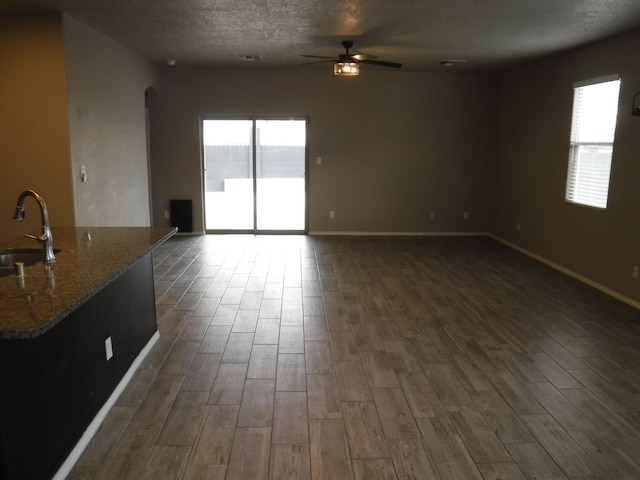 unfurnished living room featuring arched walkways, a sink, baseboards, ceiling fan, and dark wood-type flooring
