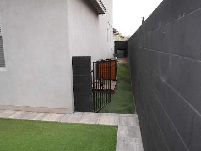 view of side of home with stucco siding, a gate, fence, and central AC