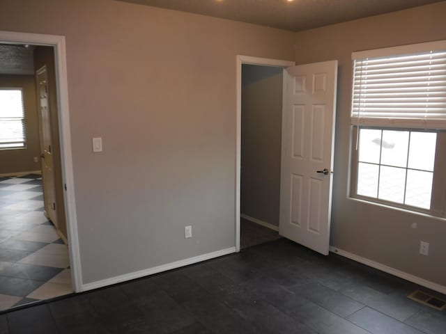 empty room with baseboards, dark tile patterned floors, and visible vents