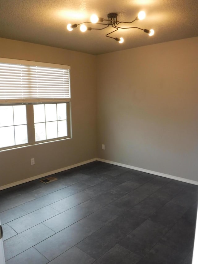 spare room featuring baseboards, dark tile patterned flooring, visible vents, and a textured ceiling
