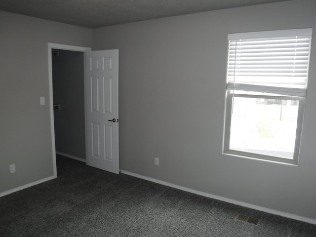 empty room featuring baseboards, dark colored carpet, and visible vents