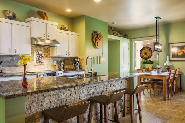 kitchen with stove, a kitchen breakfast bar, under cabinet range hood, a sink, and decorative backsplash