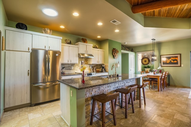 kitchen featuring freestanding refrigerator, a breakfast bar, under cabinet range hood, a kitchen island with sink, and a sink