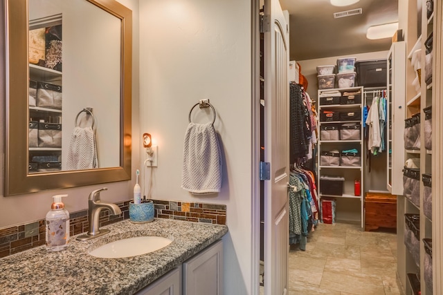 bathroom featuring tasteful backsplash, vanity, a spacious closet, stone finish flooring, and visible vents