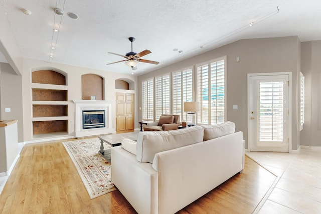 4104 Killington Rd NW, Albuquerque, NM 87114 - living room featuring built in features, ceiling fan, a textured ceiling, baseboards, and a glass covered fireplace
