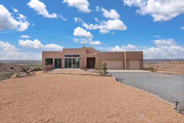 pueblo-style home with gravel driveway, stucco siding, and an attached garage