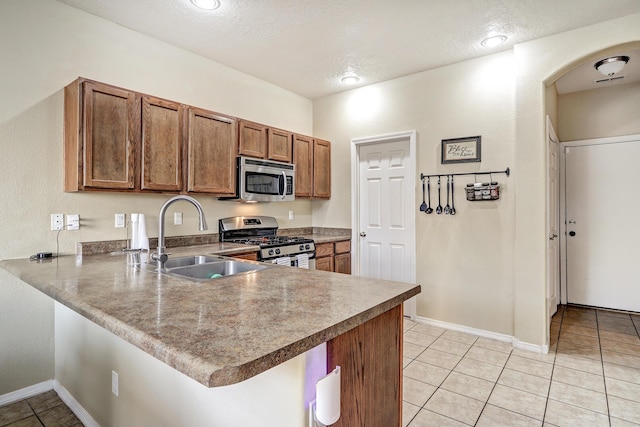 2467 Corvara Dr SE, Rio Rancho, NM 87124 - kitchen with appliances with stainless steel finishes, a sink, a peninsula, brown cabinetry, and light tile patterned floors