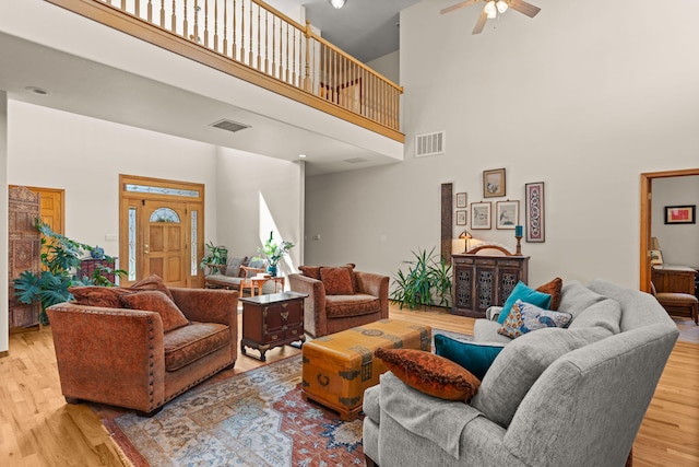 living room featuring a high ceiling, light wood finished floors, a ceiling fan, and visible vents