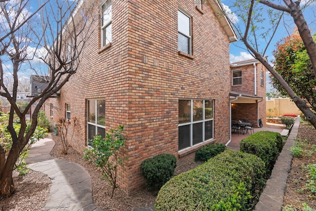 view of side of home with brick siding, fence, and a patio area