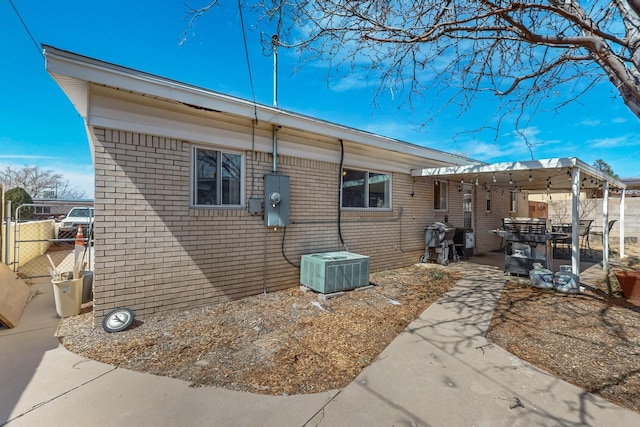 view of side of home with central AC unit, fence, brick siding, and a patio