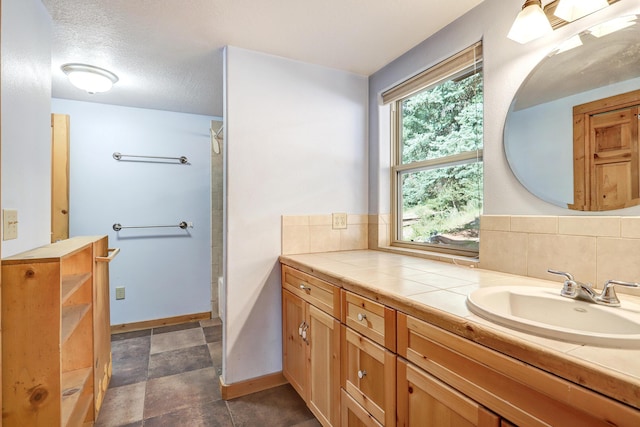 full bath with vanity, backsplash, a textured ceiling, walk in shower, and baseboards