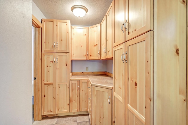 kitchen featuring a textured ceiling, tile countertops, and light brown cabinetry