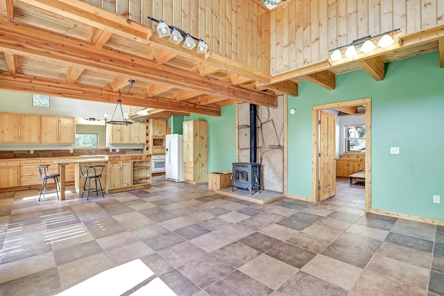 unfurnished living room with wooden ceiling, beam ceiling, a wood stove, baseboards, and an inviting chandelier