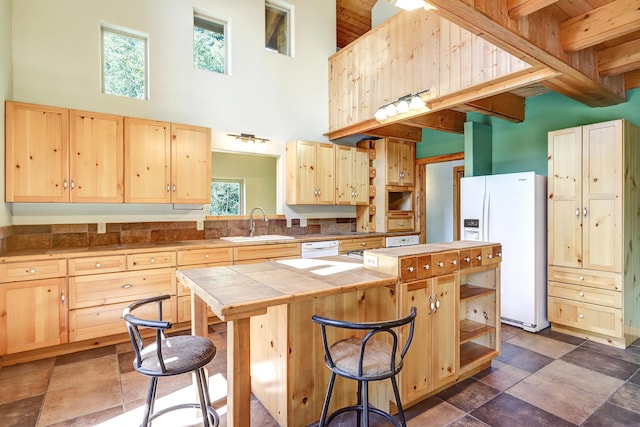 kitchen featuring white appliances, light brown cabinets, a sink, a high ceiling, and a center island