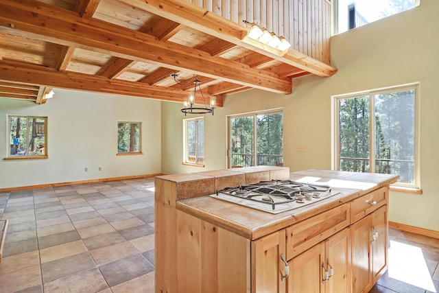 kitchen with white gas cooktop, beamed ceiling, baseboards, tile countertops, and light brown cabinetry