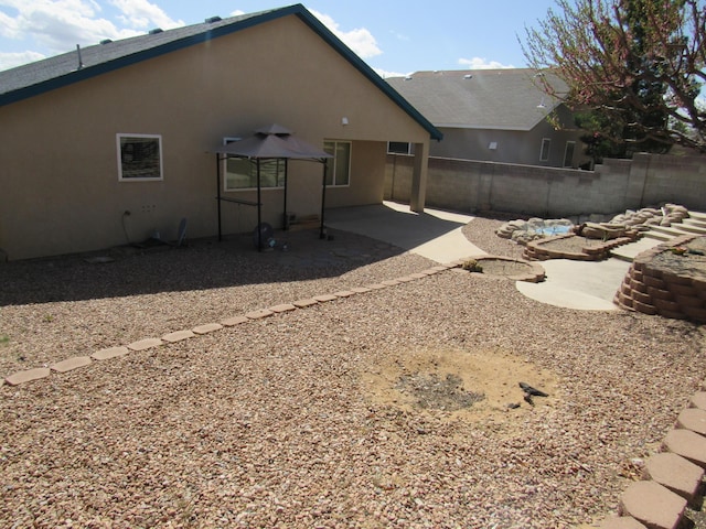 rear view of house featuring stucco siding, fence, and a patio area