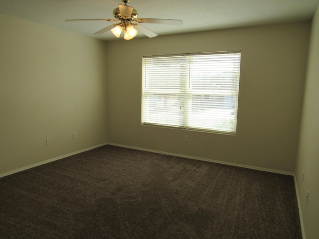 spare room featuring ceiling fan, dark carpet, and baseboards