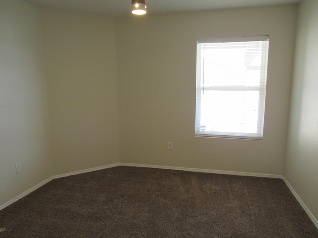 spare room featuring dark colored carpet and baseboards