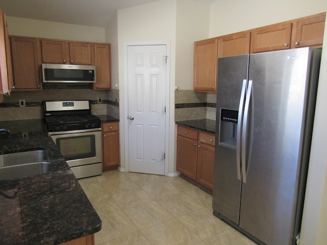 kitchen with dark stone counters, a sink, stainless steel appliances, and tasteful backsplash
