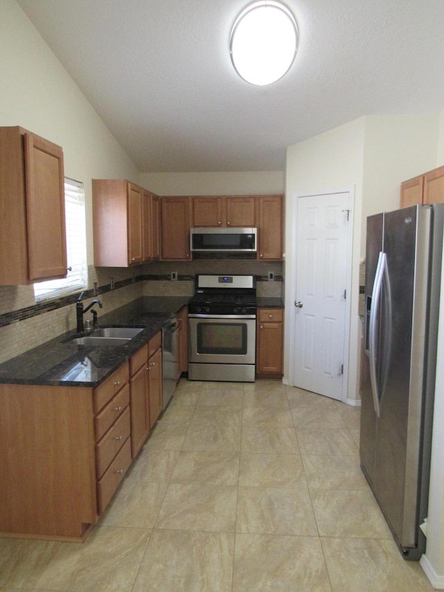 kitchen with a sink, stainless steel appliances, brown cabinetry, vaulted ceiling, and backsplash