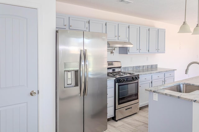 kitchen with light stone countertops, under cabinet range hood, appliances with stainless steel finishes, a sink, and pendant lighting