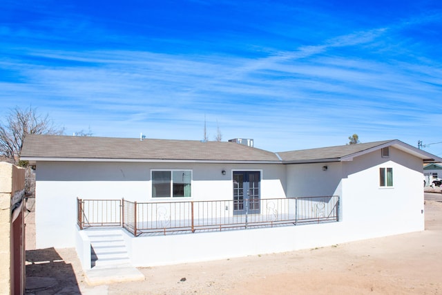 rear view of house featuring stucco siding and roof with shingles