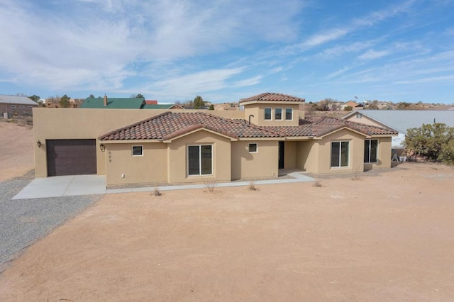 mediterranean / spanish house featuring stucco siding, a tiled roof, gravel driveway, and a garage