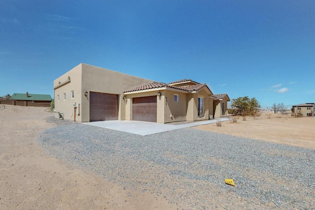 southwest-style home featuring gravel driveway, a garage, and stucco siding