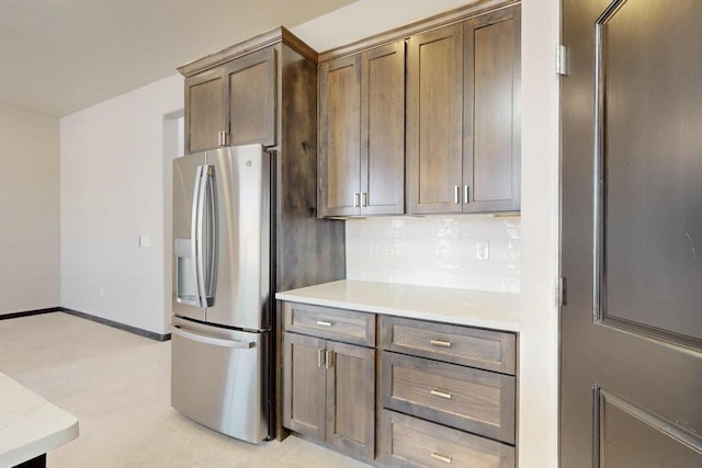 kitchen with baseboards, stainless steel refrigerator with ice dispenser, light countertops, and decorative backsplash