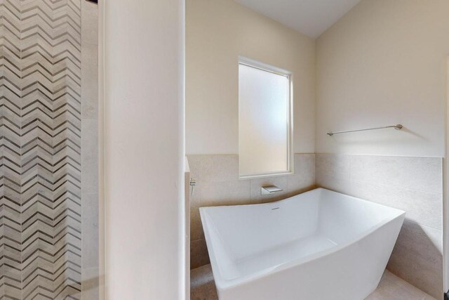 full bathroom with tile walls, a freestanding bath, and wainscoting