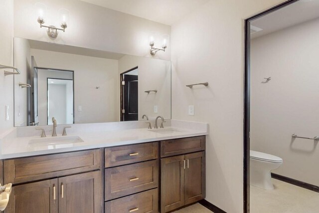 bathroom featuring double vanity, toilet, baseboards, and a sink