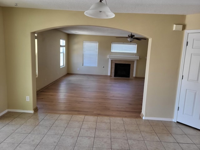 1511 White Pine Dr, Rio Rancho, NM 87144 - unfurnished living room with a ceiling fan, arched walkways, light wood-style floors, a tile fireplace, and a textured ceiling