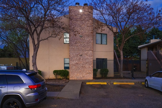 view of home's exterior featuring a chimney, fence, stucco siding, uncovered parking, and brick siding