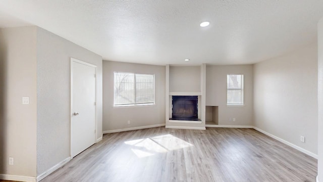unfurnished living room with a wealth of natural light, light wood-style floors, a fireplace with raised hearth, and baseboards