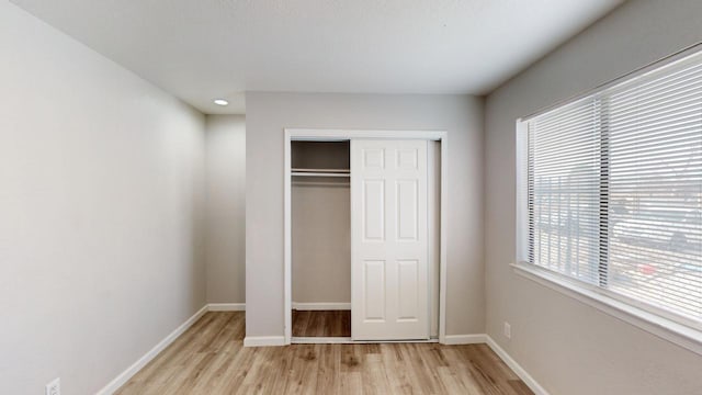 unfurnished bedroom with light wood-style flooring, a closet, and baseboards
