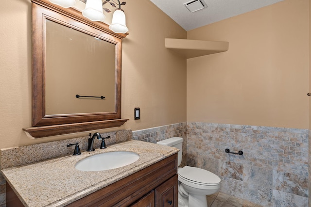 bathroom featuring tile walls, toilet, vanity, tile patterned floors, and wainscoting