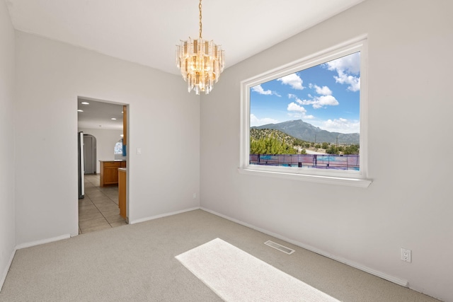 spare room featuring light carpet, a mountain view, a chandelier, and baseboards