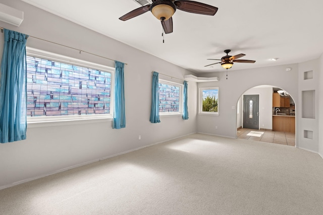 spare room featuring a ceiling fan, arched walkways, light colored carpet, and baseboards