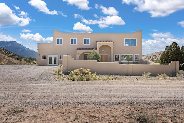 pueblo-style house with stucco siding, a fenced front yard, french doors, and a mountain view
