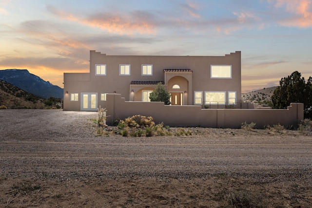 pueblo-style home with a fenced front yard, stucco siding, french doors, and a mountain view