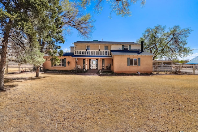 rear view of property featuring fence, stucco siding, and a balcony