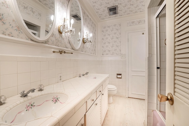bathroom featuring wallpapered walls, toilet, wainscoting, a sink, and wood finished floors