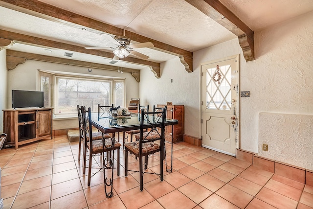 dining space featuring a textured ceiling, a textured wall, beamed ceiling, and plenty of natural light