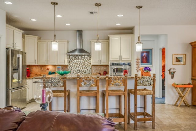 kitchen featuring wall chimney range hood, light stone countertops, decorative backsplash, and appliances with stainless steel finishes