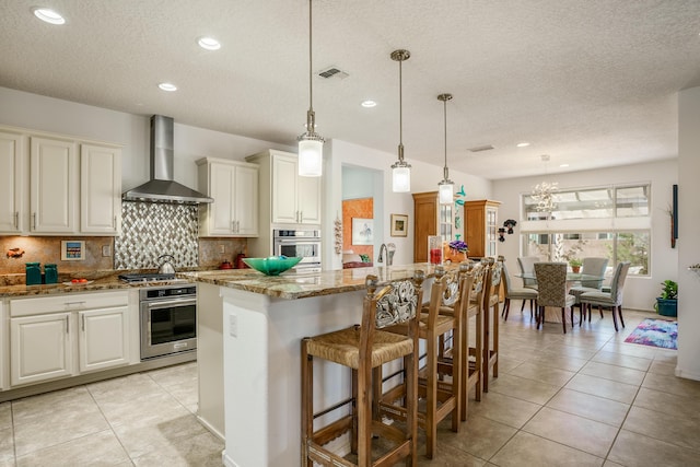 kitchen featuring decorative backsplash, oven, wall chimney range hood, and light tile patterned floors