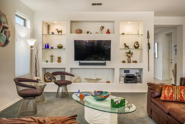 carpeted living area featuring baseboards, visible vents, a textured ceiling, and built in features