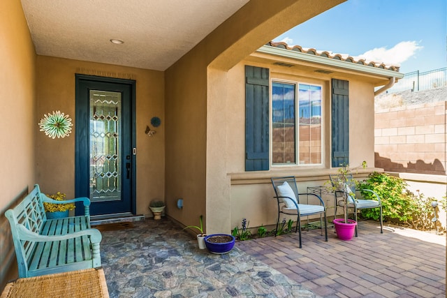view of exterior entry with a patio area, stucco siding, and fence