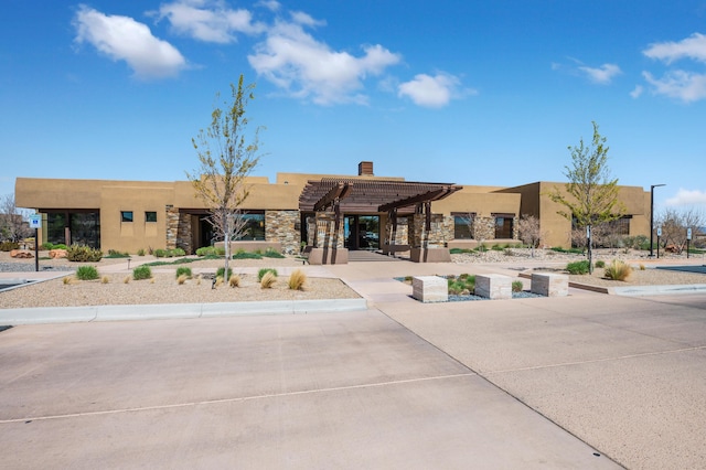 view of front facade with a chimney, a pergola, stone siding, and stucco siding