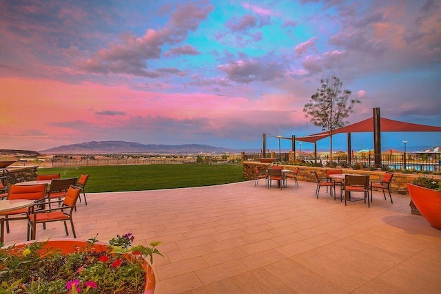 patio terrace at dusk featuring a mountain view and a lawn