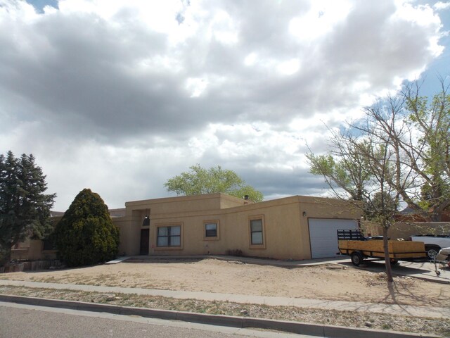 12900 Piru Blvd SE, Albuquerque, NM 87123 - pueblo-style house with an attached garage, concrete driveway, and stucco siding